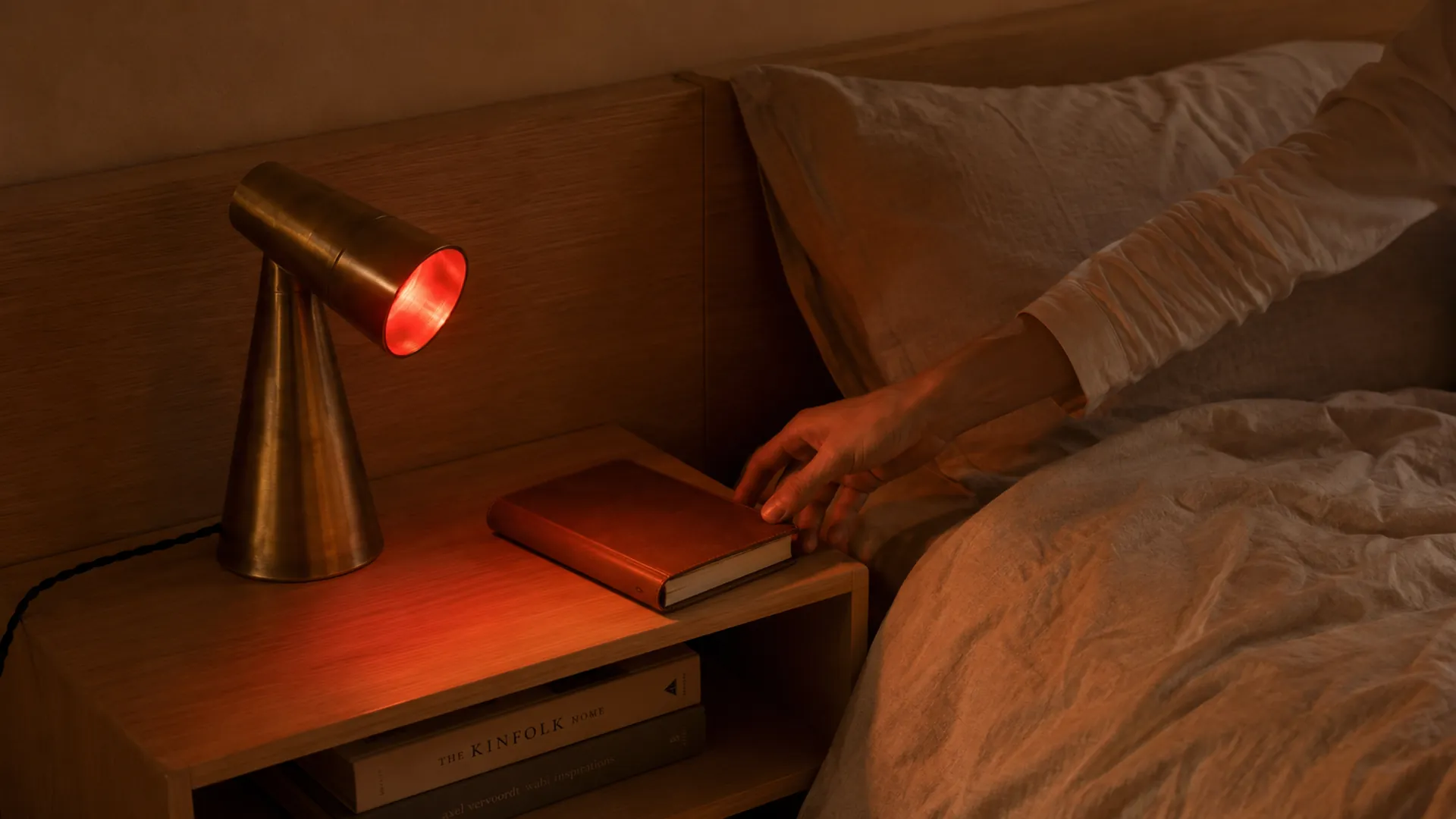 Milieu lamp red-lit on a bedside table, hand reaching for a book